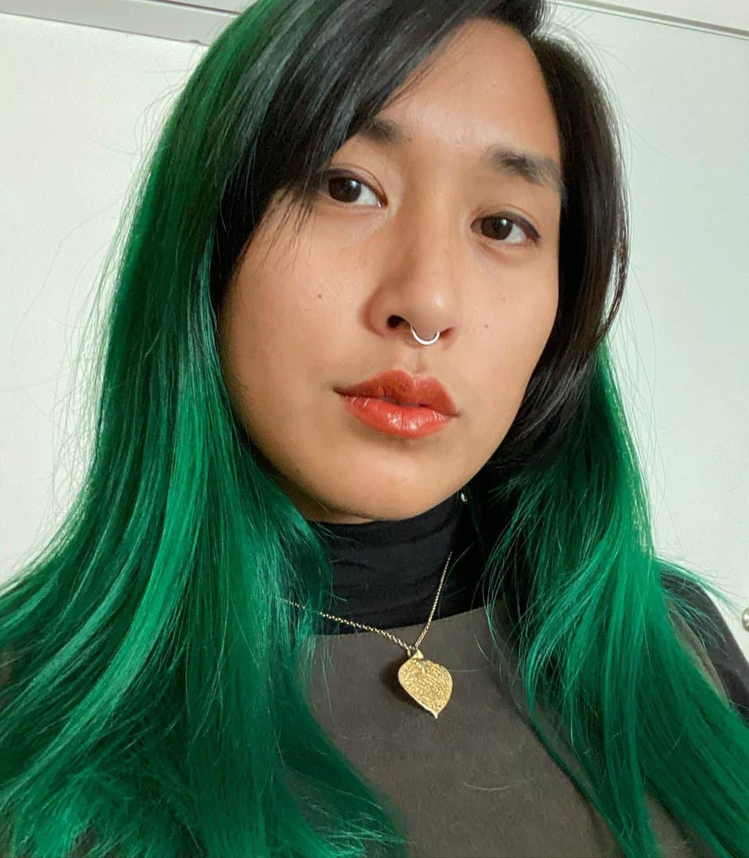 Mia Littleのインスタグラム：「A fresh green self dye to keep my spirits up on this godforsaken platform. [pd: Head shot of Mia looking into the camera wearing minimal makeup—faint eye liner and burnt pumpkin colored lip stain. They have vibrant green ombre hair and black bangs and roots. Mia is wearing a black turtleneck layered under a olive green suede shift dress and is wearing a gold necklace with a gold leaf pendant.]」