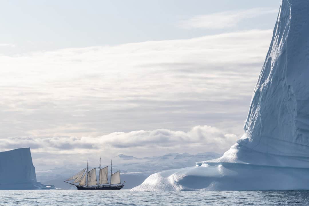 National Geographic Travelのインスタグラム：「Photo by @daisygilardini / During my latest expedition to Greenland’s Scoresby Sound, we decided to photograph our ship—the 94-year-old, three-masted schooner Rembrandt van Rijn—sailing among icebergs. What looked to be an easy task at first turned out to be a demanding and time-consuming challenge. The Rembrandt is a tall ship, a traditionally rigged sailing vessel, which means all the sails have to be lifted manually without electrical winches. Once the sails are up, the challenge is to board a Zodiac while the ship is moving. Then you hope for a bit of breeze so the sails are nicely rounded and some photogenic icebergs, both in the foreground and background. After an hour or so of bouncing around in the Zodiac, feeling dizzy and seasick, it all came together!  Follow me @daisygilardini for more images and behind-the-scenes stories. #greenland #ship #iceberg #arctic #climatechange」